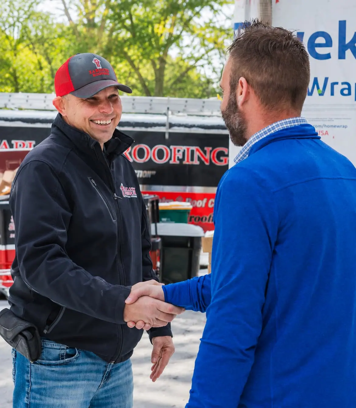 A Zablocki Roofing team member shaking hands with a satisfied customer in front of the company truck